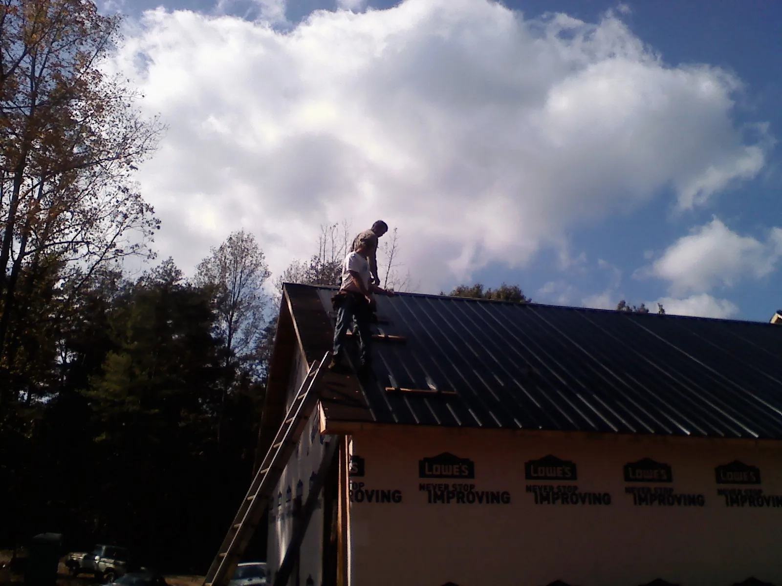 Roofer fastening dark metal panels high against a cloudy sky, from a Roof Inspection job in Asotin