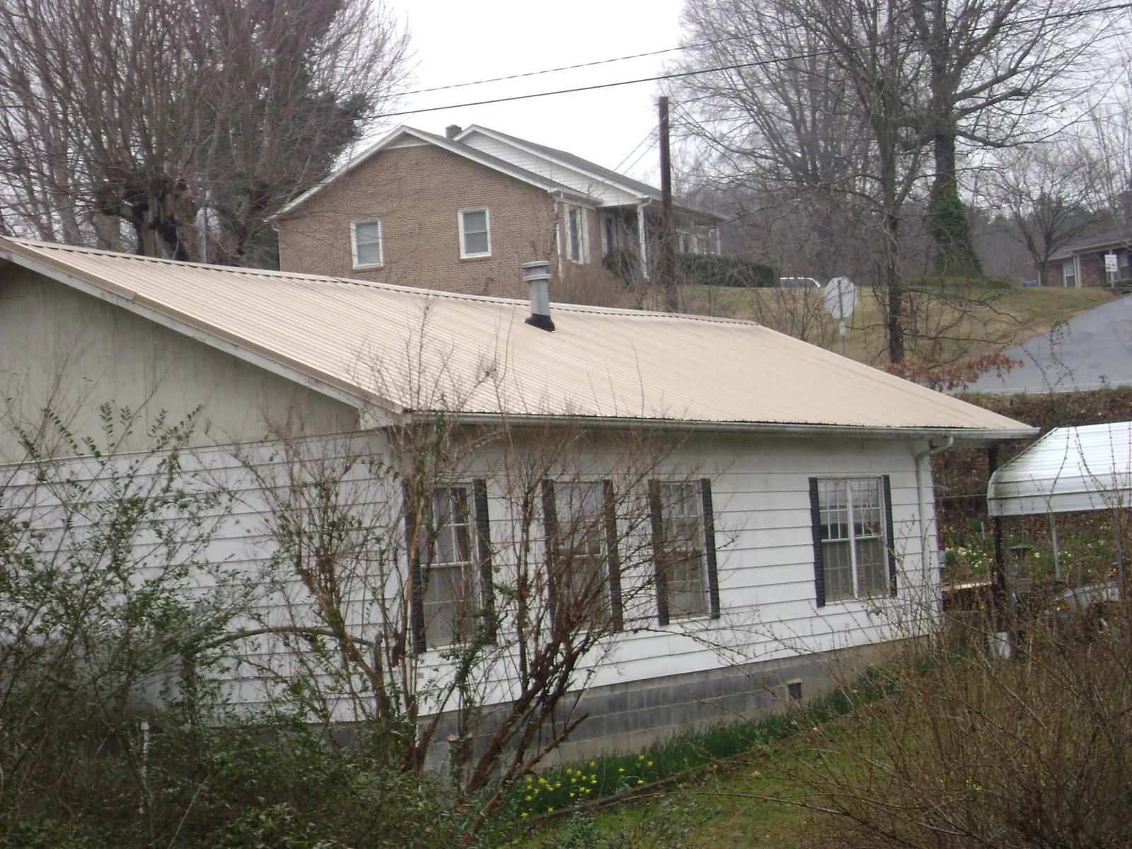 Tan metal roof on a white sided house set into a hillside — Commercial Roofing by Roofing Brothers in Asotin